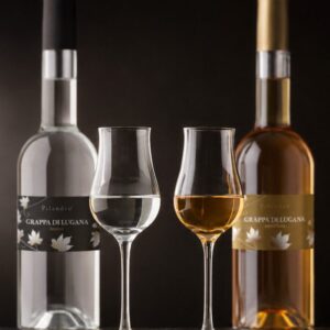 Zwei Grappagläser zwischen ihren Flaschen, farblos und bernstein – Grappa di Lugana Tardiva und Invecchiata aus Turbiana von Pilandro, Desenzano